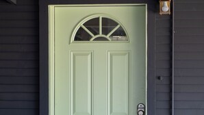Une porte vert clair avec une petite fenêtre au-dessus, une poignée de porte et une boîte aux lettres sur le côté droit.
