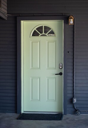 A light green door with a small window above it, a doorknob, and a mailbox on the right side.