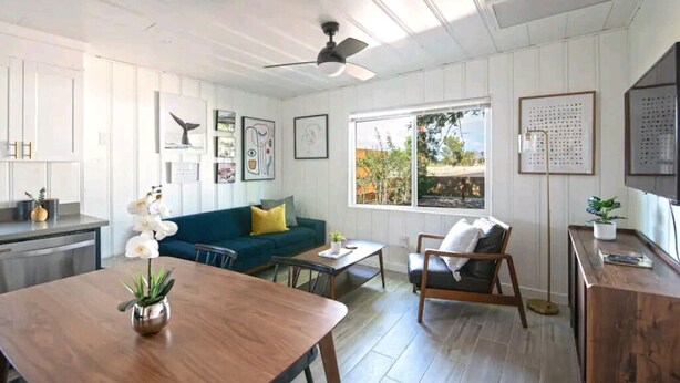 Un salon spacieux avec une table à manger en bois, un canapé bleu, une table basse et un ventilateur de plafond.