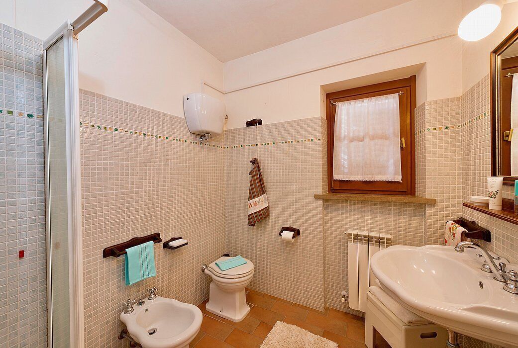 Ein Badezimmer mit einem Bidet, WC, Waschbecken und einem Fenster mit Vorhang.