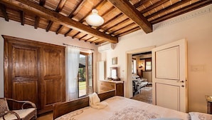 Un dormitorio con techo de madera, una cama con colcha estampada, un armario de madera y una ventana con cortinas.