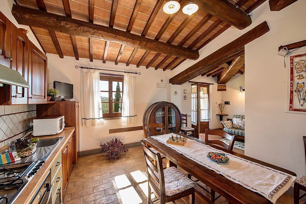 Una cocina rústica con vigas de madera, una mesa de comedor con sillas, una estufa y un televisor.