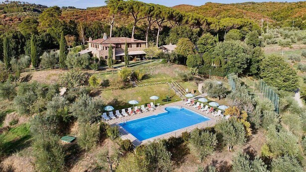 A large house with a swimming pool surrounded by trees and a hilly landscape.