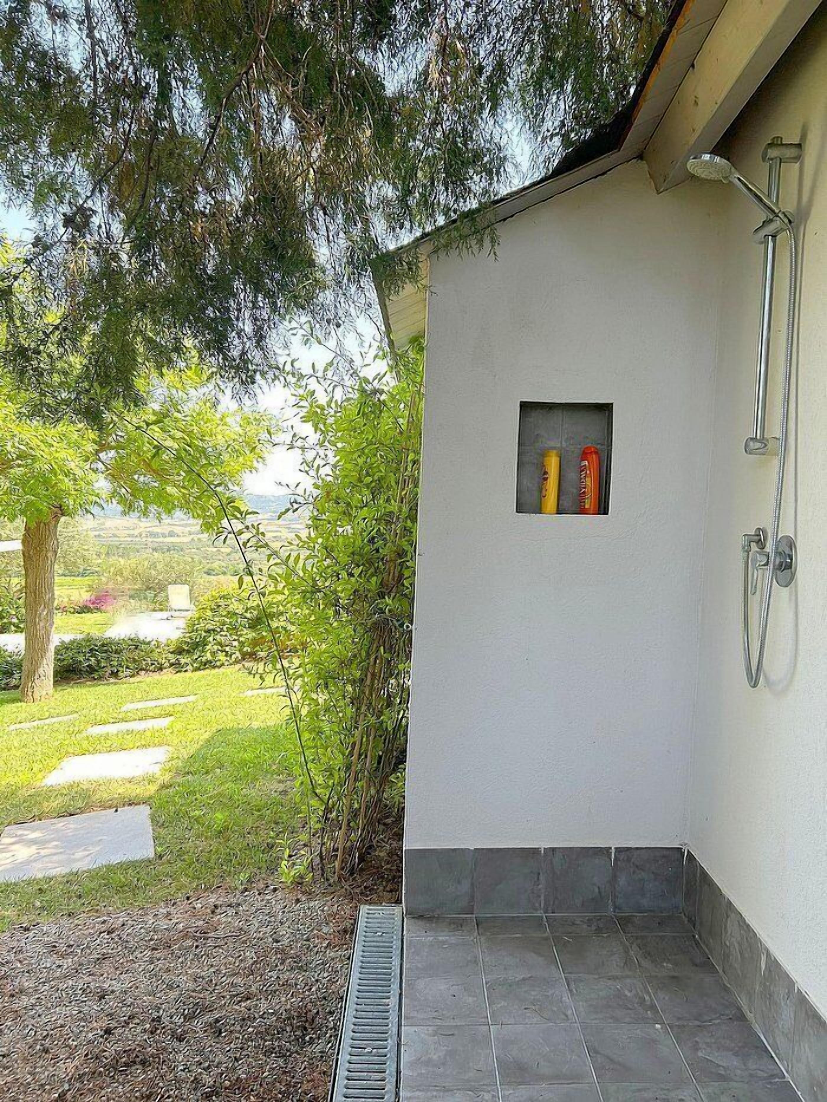 A small, enclosed shower area with a tiled floor and a window with toiletries.