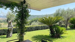 An outdoor seating area with a table and chairs, surrounded by lush greenery and a view of the countryside. - Villa Bougainville: A welcoming one-story villa situated in a quiet location, a few minutes from the town center, with Free WI-FI. (Amaroni)