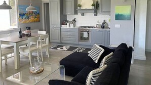A modern kitchen with grey cabinets, a dining area with white chairs, and a black sofa with patterned cushions. - Villa Bougainville: A welcoming one-story villa situated in a quiet location, a few minutes from the town center, with Free WI-FI. (Amaroni)