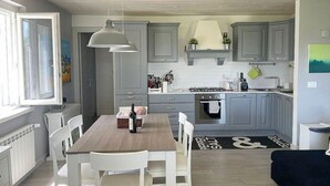 A modern kitchen with grey cabinets, a wooden dining table, and a black and white rug. - Villa Bougainville: A welcoming one-story villa situated in a quiet location, a few minutes from the town center, with Free WI-FI. (Amaroni)