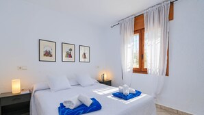 A neatly arranged bedroom with a bed, two bedside tables, a window with curtains, and three framed pictures on the wall. - Milugar - Javea, Costa Blanca (Javea)