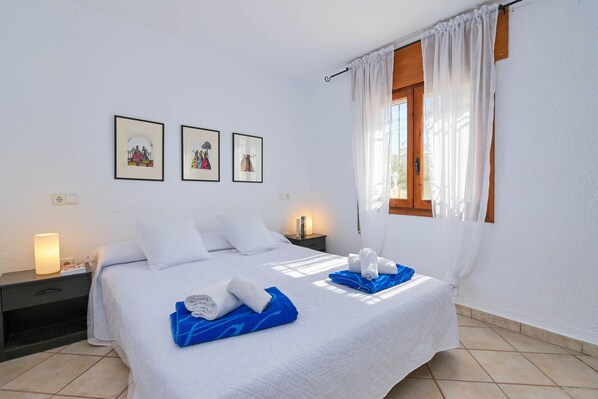 A neatly arranged bedroom with a bed, two bedside tables, a window with curtains, and three framed pictures on the wall.
