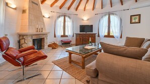 A living room with a fireplace, leather chair, sofa, and a TV. - Milugar - Javea, Costa Blanca (Javea)