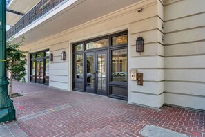 A building with a brick-paved entrance, large glass doors, and a balcony with metal railings. - St Charles Ave Condo | Streetcars, Parking, Pool! (New Orleans)