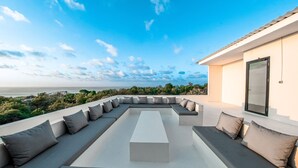 Zona relax esterna moderna con una lunga panca e cuscini, affacciata su una vista panoramica del mare e del verde.