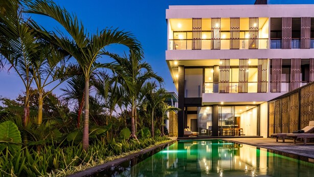 Un edificio moderno con piscina, immerso in piante tropicali.