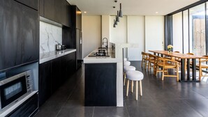Una cucina moderna con mobili scuri, una schienale in marmo e un'isola centrale con sgabelli.