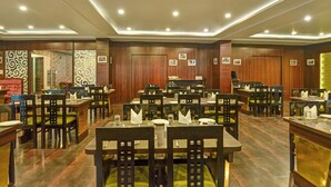 Restaurante com várias mesas e cadeiras, painéis de madeira nas paredes e luminárias no teto.