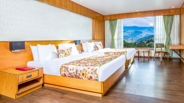 Quarto de hotel com uma cama grande, uma mesa, uma cadeira e vista para as montanhas.