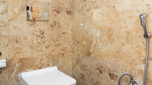 Een badkamer met een marmeren wand, een wit toilet en een douchearmatuur.
