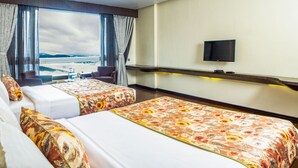 Quarto de hotel com duas camas, televisão, janela com cortinas e vista para as montanhas.
