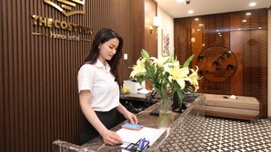 Un mostrador de recepción de hotel con un panel de pared de madera, un mostrador, un jarrón con flores y un sofá.