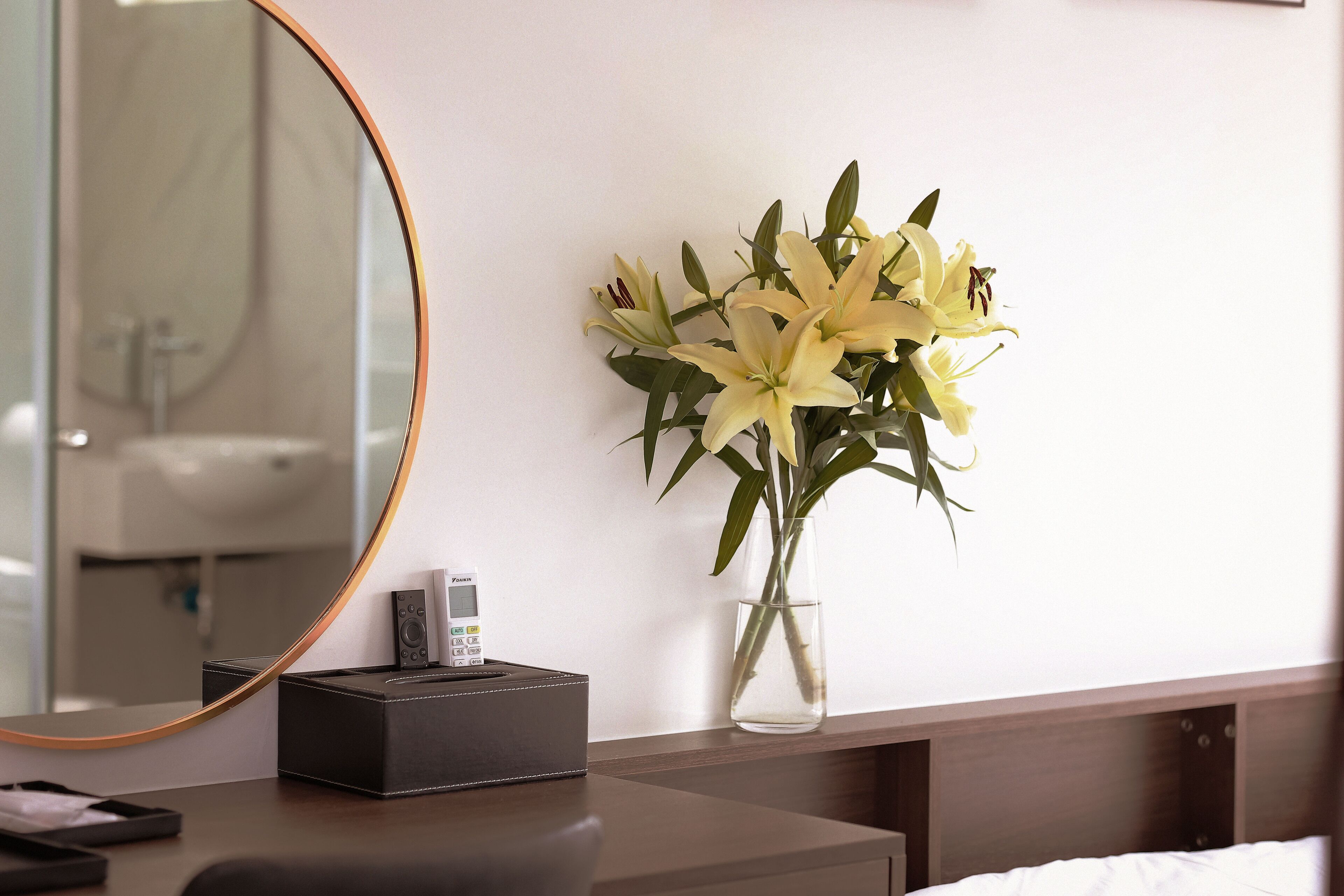 A hotel room with a bedside table, a vase with flowers, a mirror, and a small box.