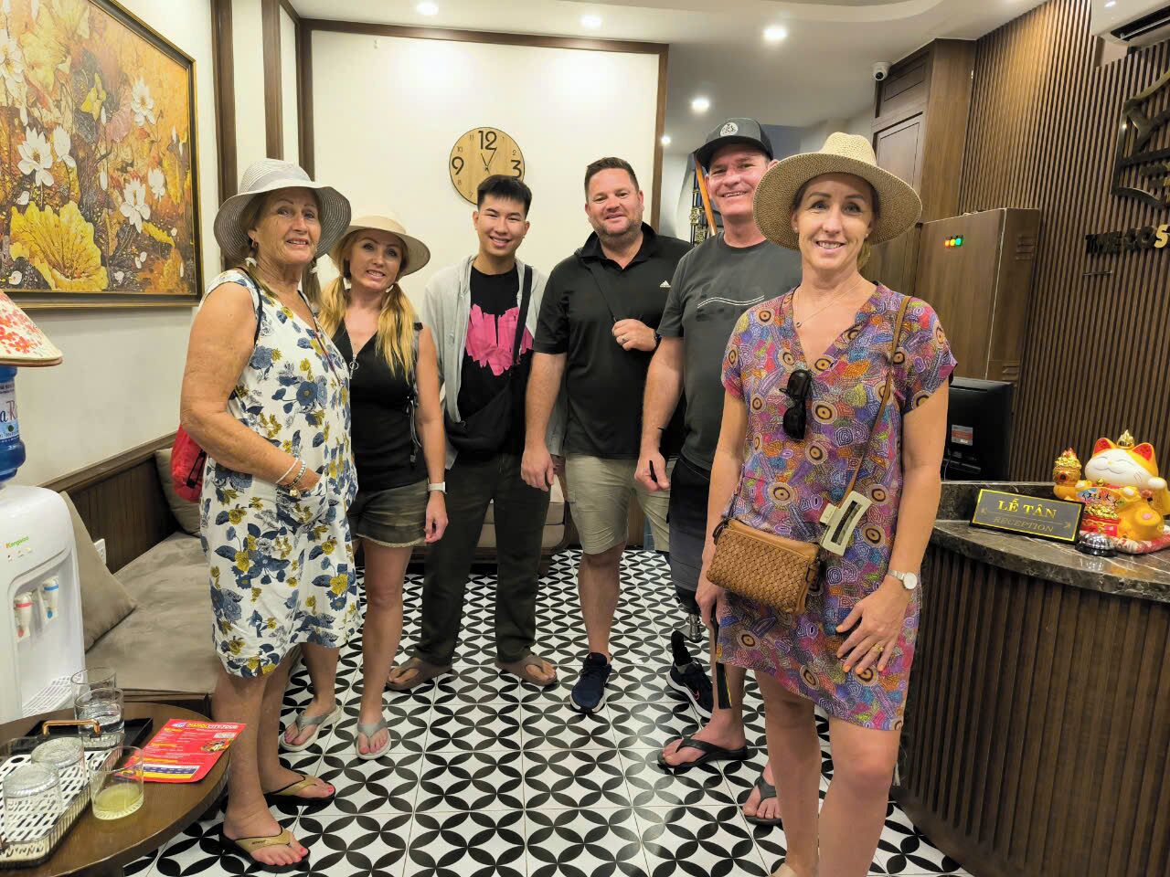 A group of people standing in a hotel lobby with a clock, a reception desk, and a water dispenser.