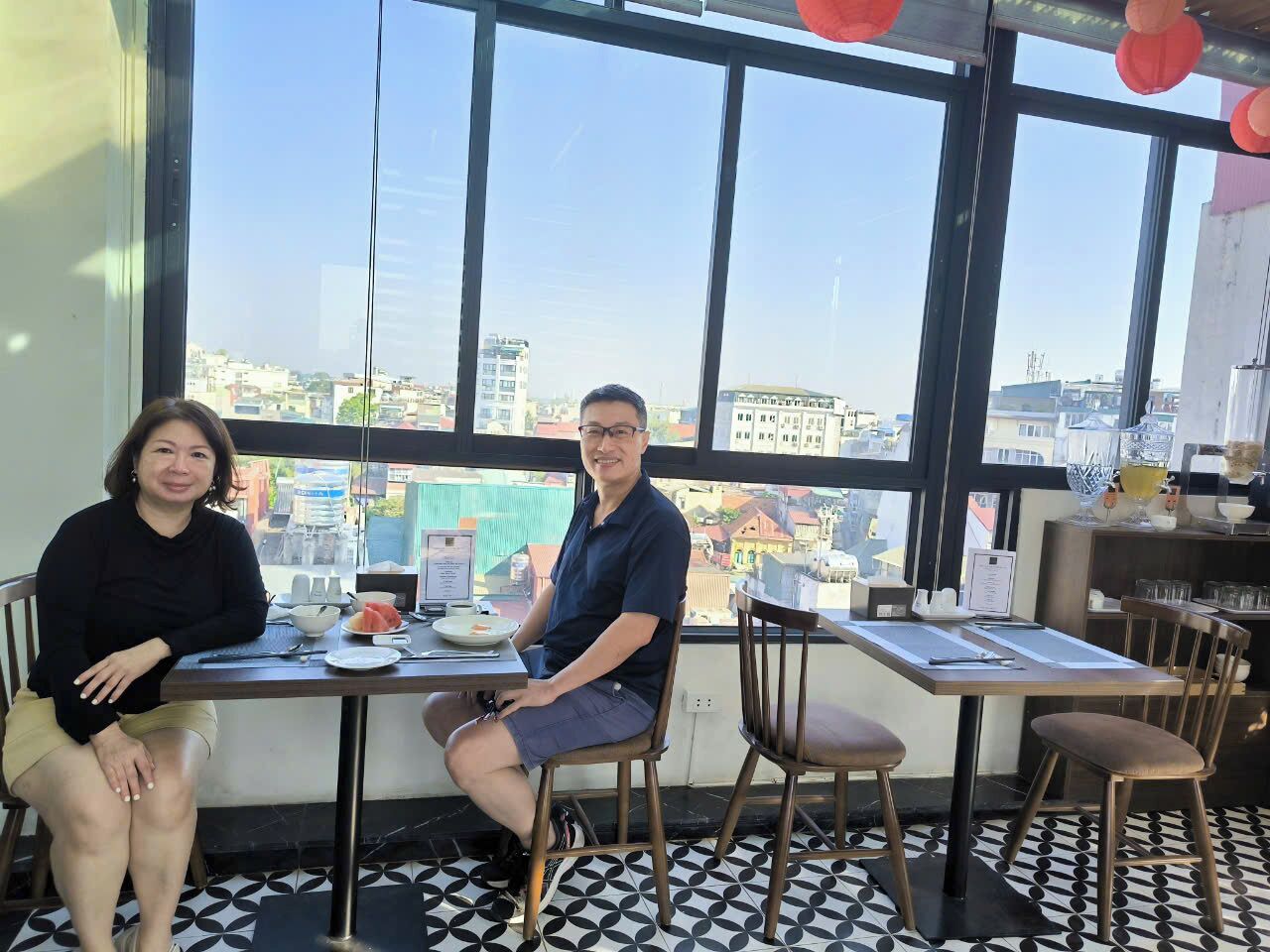 Two people seated at a table with a city view through large windows.