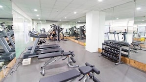 Une salle de sport équipée de tapis de course, d’appareils de musculation et d’une série de haltères.