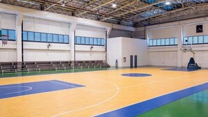 Un terrain de basket-ball intérieur doté d’un plancher en bois, de marquages bleus et verts, et de gradins le long des murs.