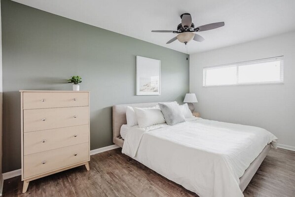 A bedroom with a bed, a dresser, a ceiling fan, a window, and a wall-mounted picture. - Calm & Peaceful 3B: King Beds by Liberty Hospital (Liberty Township)