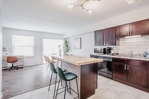 A modern kitchen with dark wooden cabinets, a central island with bar stools, a built-in oven, and a stainless steel sink. - Calm & Peaceful 3B: King Beds by Liberty Hospital (Liberty Township)