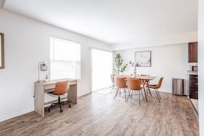 A modern, well-lit room with a wooden desk, a dining table with chairs, a small potted plant, and a framed picture on the wall. - Calm & Peaceful 3B: King Beds by Liberty Hospital (Liberty Township)
