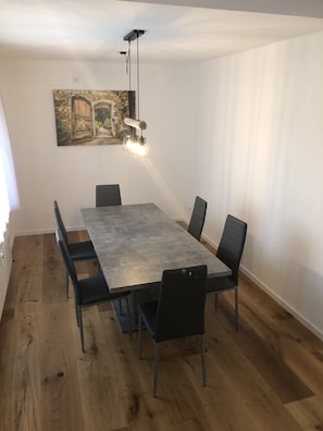 A dining area with a large rectangular table, six chairs, and a hanging light fixture. - Ferienwohnung Lolacher (Obergünzburg)