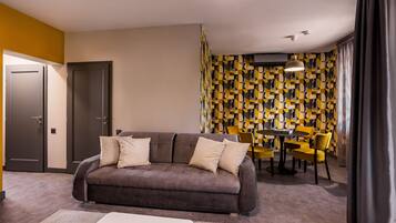A modern living room with a sofa, a dining table, and chairs. There are two doors and a patterned wall in the background.