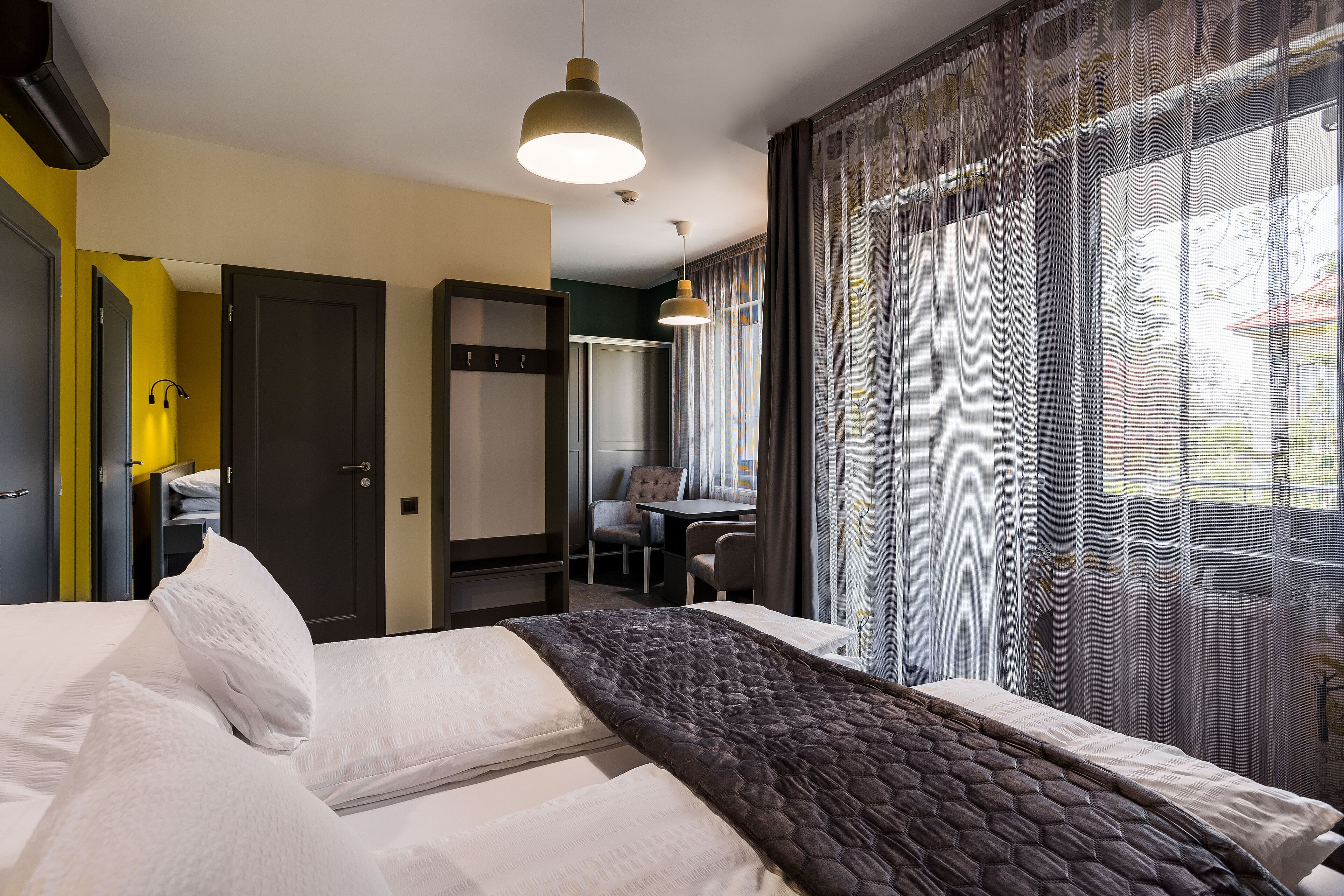 Hotelkamer met een bed, een bureau en een stoel. Een raam met gordijnen en uitzicht op buiten.