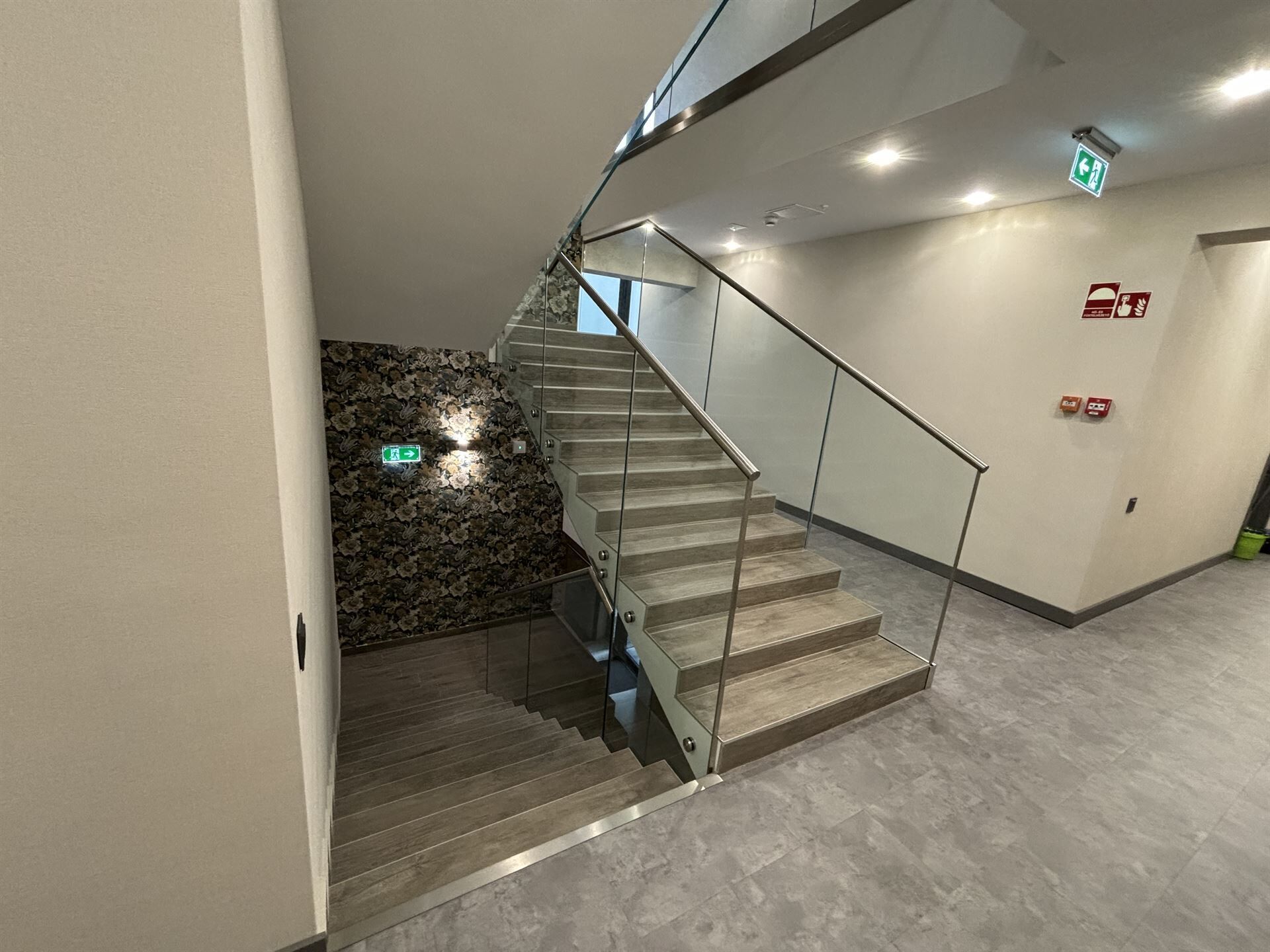 Una escalera moderna con barandas de vidrio y pared de piedra.