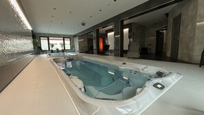 Un área de piscina interior moderna con múltiples jacuzzis y una vista despejada al exterior gracias a grandes ventanales.