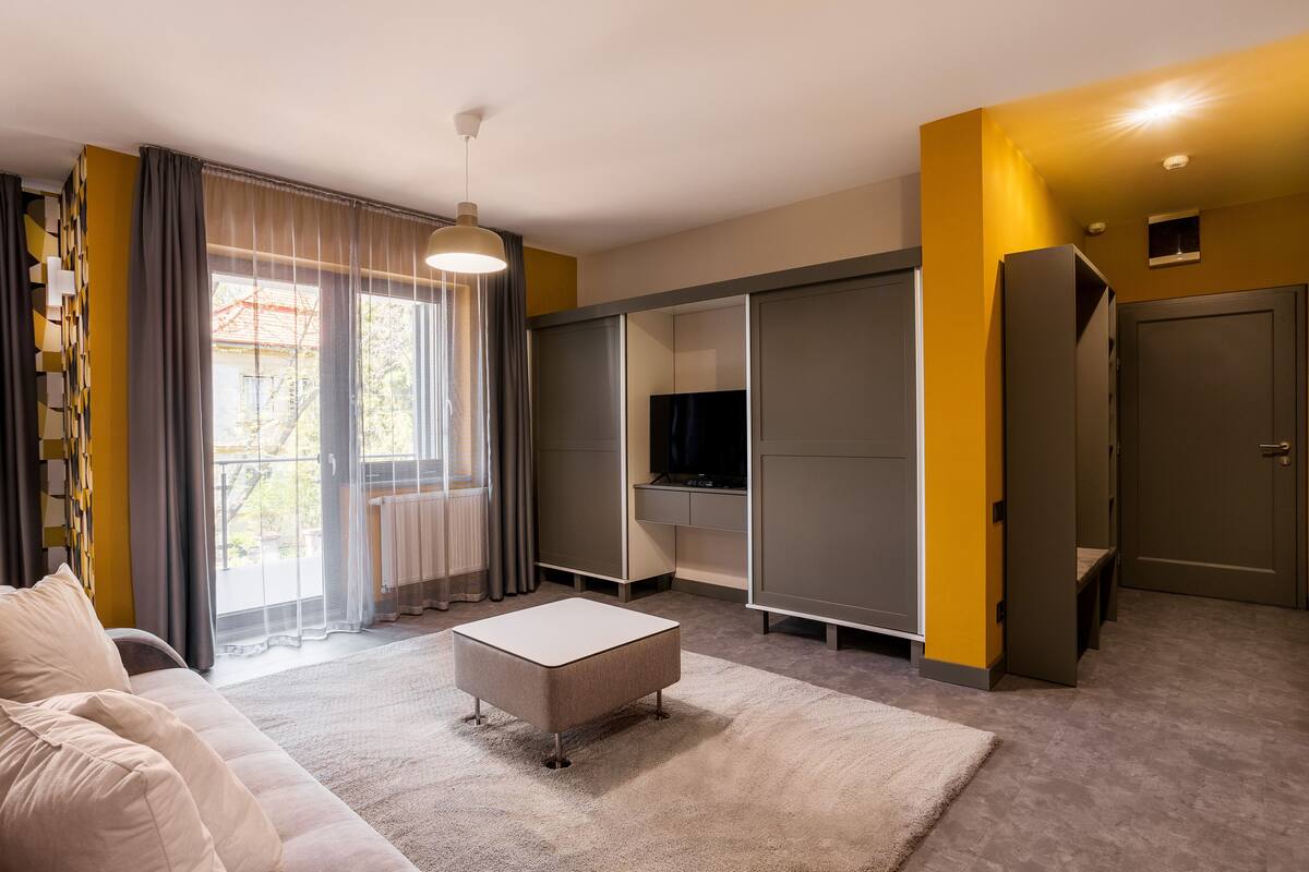 A modern living room with a sofa, ottoman, and a television on a built-in shelf.