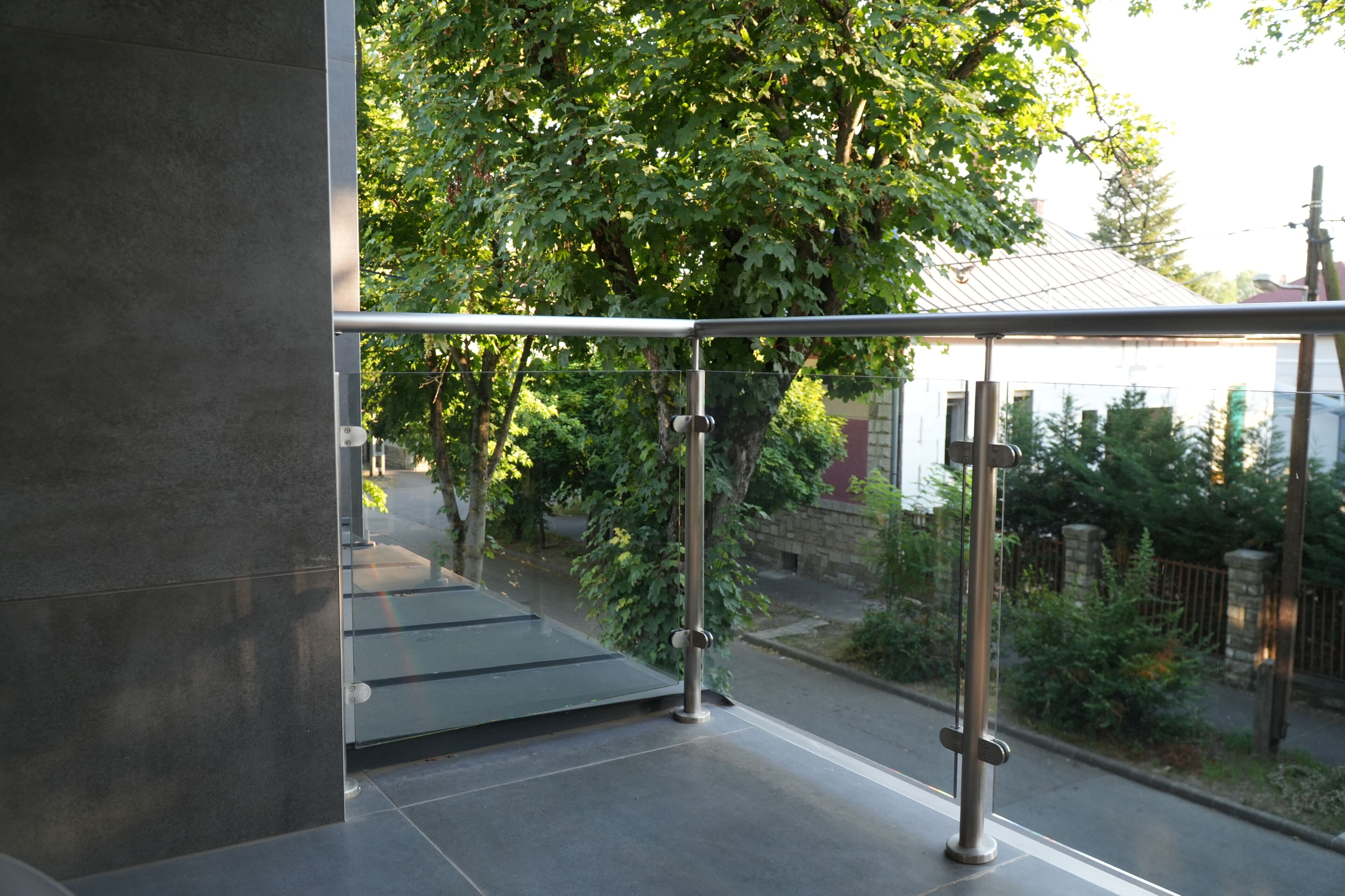 A modern building exterior with a metal railing, a glass door, and a view of a tree-lined street.