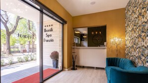 Un área de recepción con alfombra roja, un sillón color turquesa, un reloj y un papel tapiz floral.
