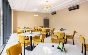 Un comedor con mesas y sillas, una araña y una puerta al fondo.