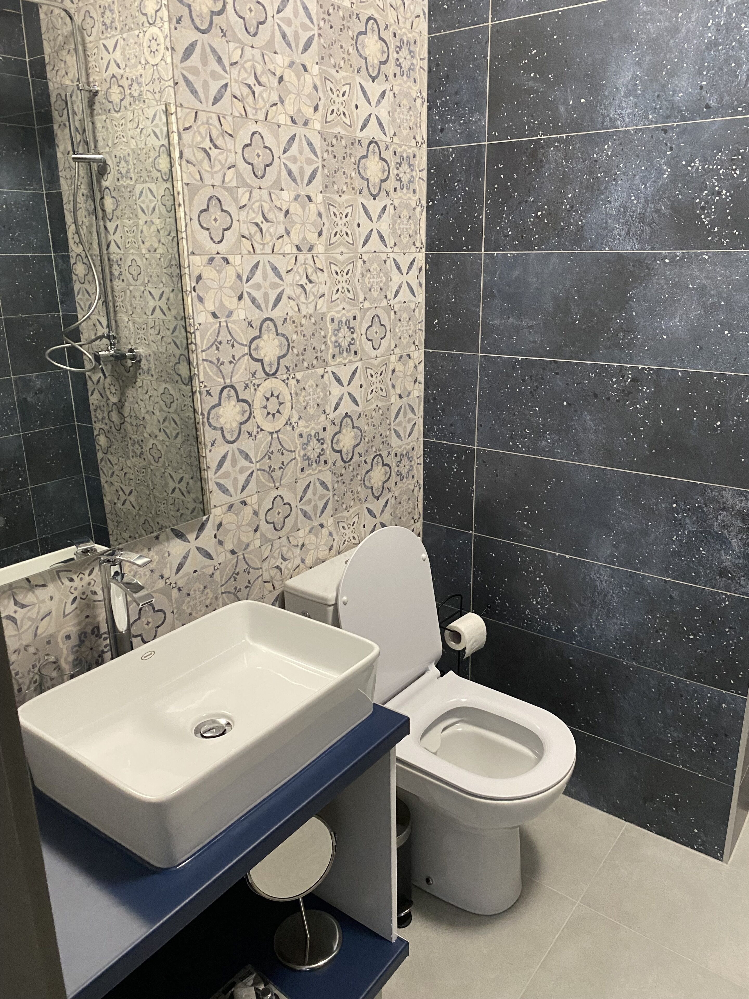 Un baño con un lavamanos blanco, un inodoro y una ducha con puerta de cristal. Las paredes están revestidas con un estampado floral.