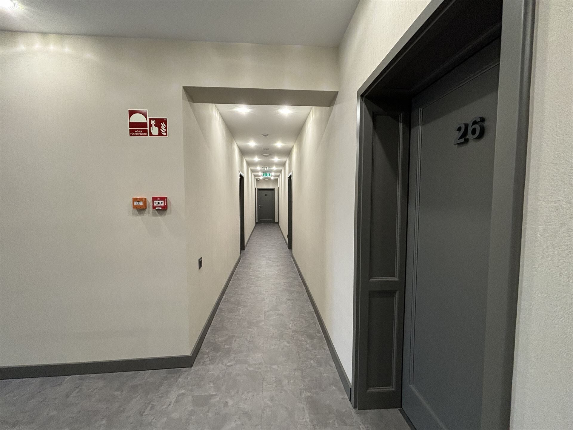 A corridor with a grey carpet, white walls, and a door marked with the number 26.