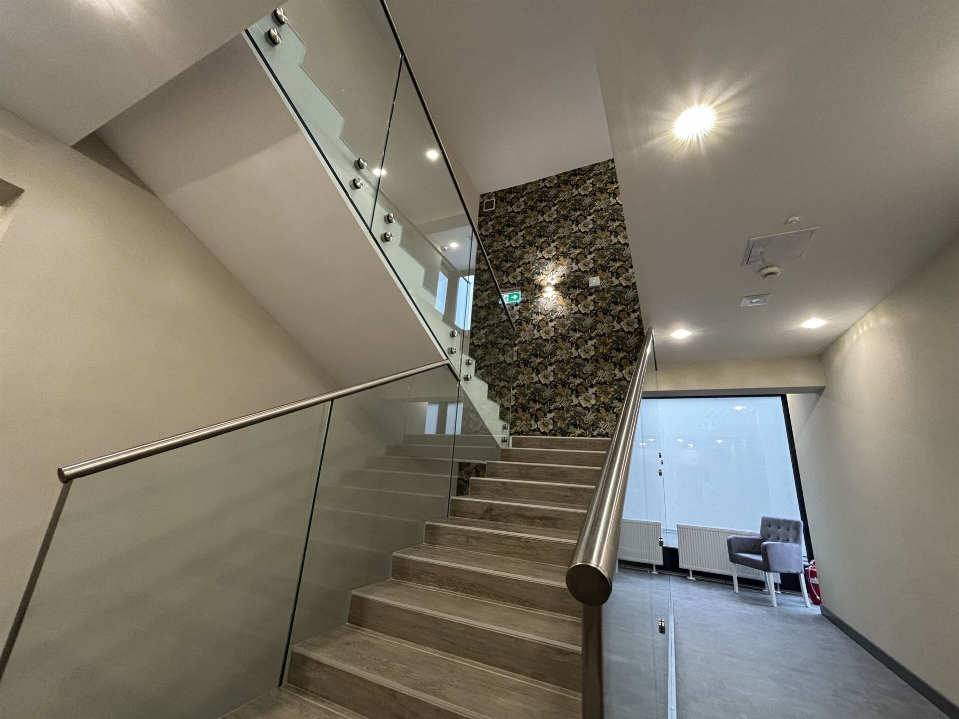 Una escalera moderna con barandillas de vidrio, peldaños de madera y un muro decorativo.