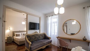 Un dormitorio con cama, sofá, sillón, espejo y televisor en la pared.