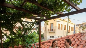 Una terraza con mesa de vidrio, sillas de mimbre y una pérgola cubierta de enredaderas.