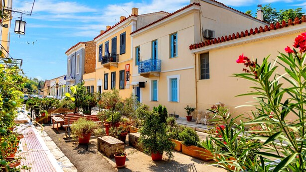 Una calle estrecha bordeada de edificios coloridos, plantas en macetas y terrazas al aire libre.