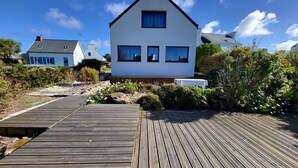 Una casa moderna con fachada blanca y una terraza de madera que lleva a la entrada.