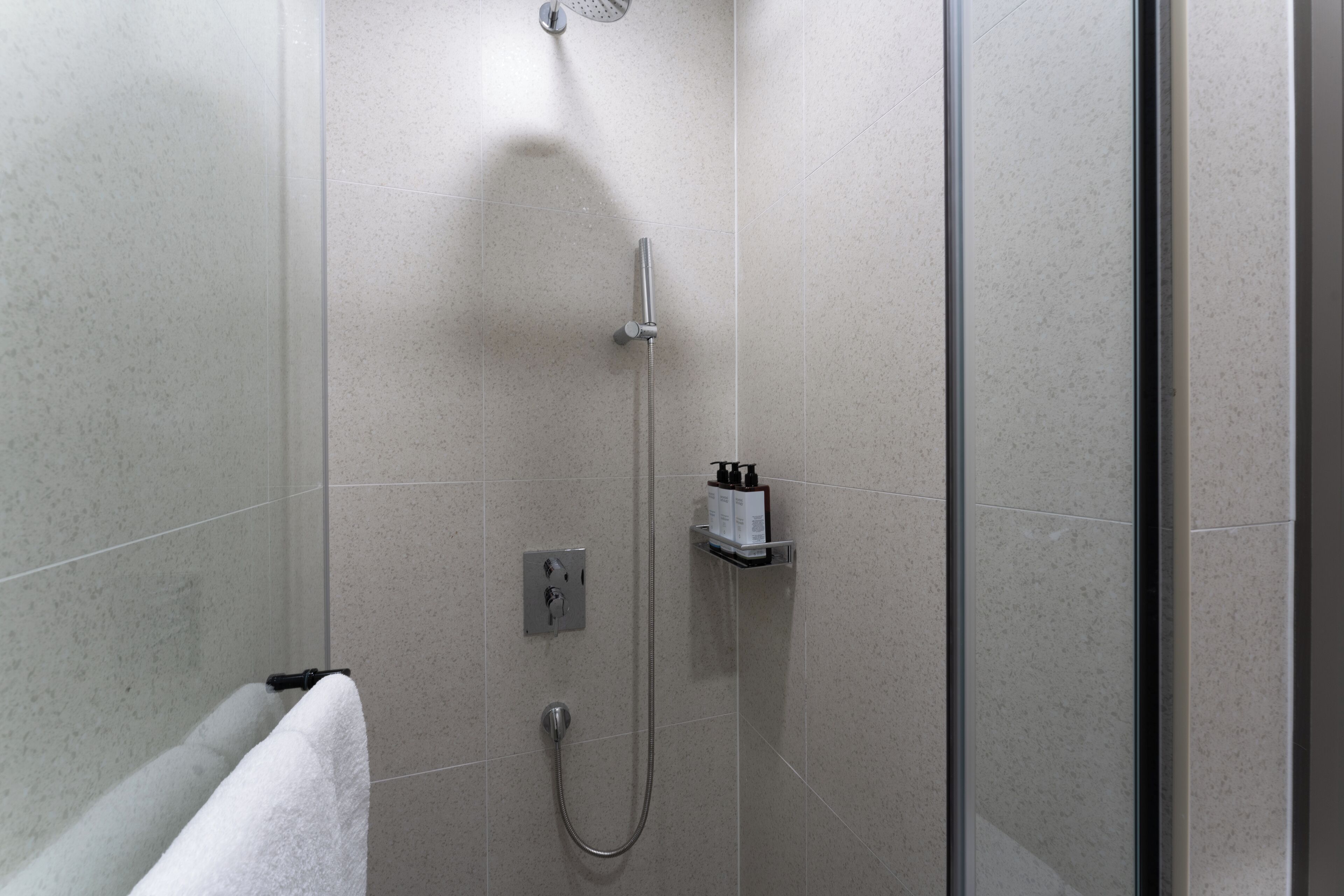 A modern bathroom with a shower, a towel rack, and a soap dispenser on the wall.