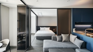 Un hotel moderno con una cama grande, un sofá gris, un comedor y vistas a la ciudad.