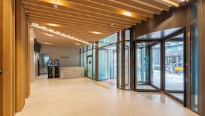 Un moderno vestíbulo de hotel con techo de madera, puertas de vidrio que dan al exterior y un mostrador de recepción.